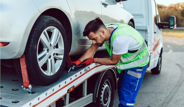 Technician performing emergency roadside and towing services kneeling down to secure wheels using the MobiWork emergency roadside assistance services software solution